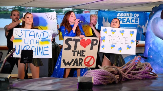 Sängerin Jasmin Wagner (aka Blümchen) zeigt mit ihren Tänzern Plakate gegen Krieg und für Frieden im Ukraine-Krieg. Etwa 40 Künstler treten im Rahmen des Projekts "Sound of Peace" unter dem Motto «Kultur für den Frieden! Stoppt die Verbrechen gegen die Menschlichkeit» auf dem Museumsschiff Rickmer Rickmers auf.  Foto: Jonas Walzberg