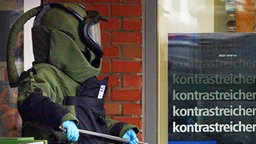 Ein Sprengstoffspezialist der Polizei trägt einen verdächtigen Fund aus einem Haus © dpa Foto: Jens Holgerson