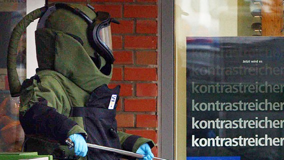 Ein Sprengstoffspezialist der Polizei trägt einen verdächtigen Fund aus einem Haus © dpa Foto: Jens Holgerson