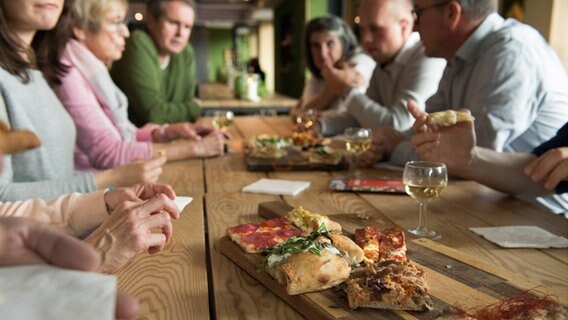 Personen sitzen um einen Tisch auf dem Tapas auf einem Holzbrett gereicht werden. © eat the world 