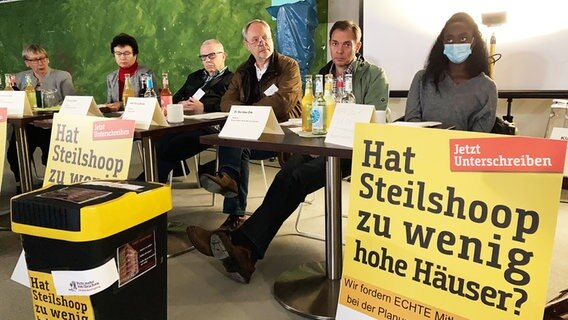 Personen sitzen an einem Tisch. Vor Ihnen stehen Plakate mit dem Schriftzug "Hat Steilshoop zu wenig Häuser". © NDR Foto: Reinhard Postelt