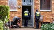 Polizisten stehen im Stadtteil Stellingen vor einem Mehrfamilienhaus. Eine Hundertjährige soll dort von ihrem Enkel getötet worden sein. © Daniel Bockwoldt/dpa 