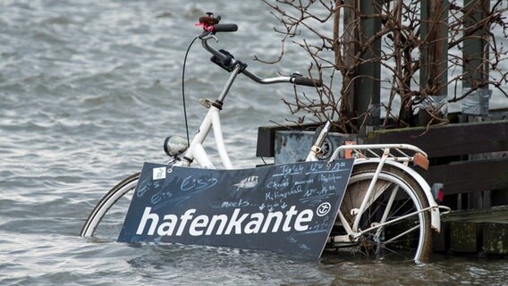 Ein Fahrrad steht während einer Sturmflut beim Hochwasser der Elbe auf dem überschwemmten Fischmarkt in Hamburg. © picture alliance / dpa Foto: Daniel Bockwoldt