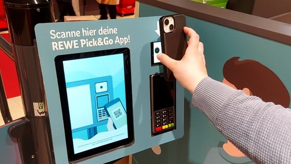Eine Person hält ein Smartphone an ein Gerät in einem Rewe-Supermarkt in Hamburg. © NDR 