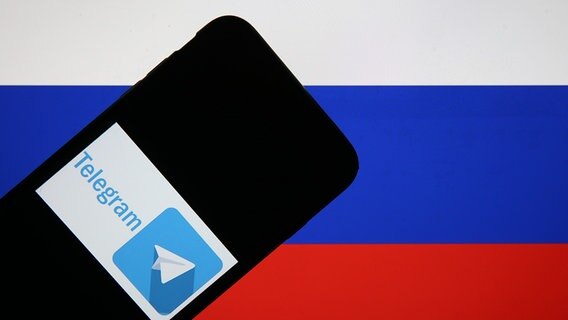 Auf einem Smartphone vor einer russischen Flagge ist ein Telegram-Symbol zu erkennen. © picture alliance / AA Foto: Rasit Aydogan