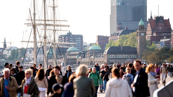 Spaziergänger sind im Sonnenschein an den Hamburger Landungsbrücken am Hafen an der Elbe unterwegs. © picture alliance/dpa Foto: Daniel Bockwoldt