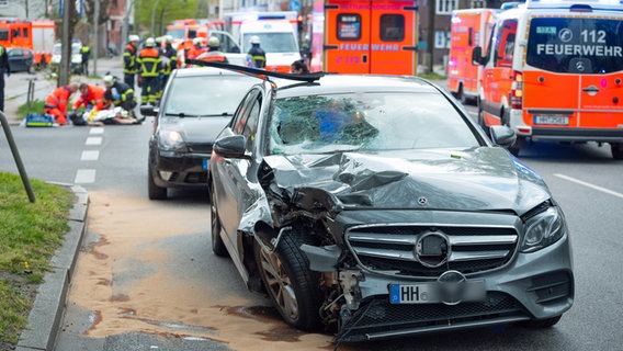 Ein beschädigter Mercedes steht nach einem Unfall auf der Kieler Straße in Hamburg, während Rettungskräfte im Hintergrund die Opfer versorgen. © picture alliance / dpa Foto: Jonas Walzberg