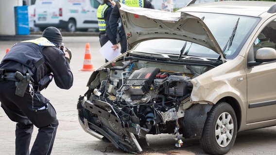 Ein Polizist fotografiert den einen Unfallwagen in Hamburg. © picture alliance / dpa Foto: Jonas Walzberg