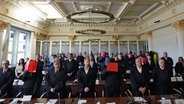Die Angeklagten stehen neben ihren Anwälten im Prozess um Vergewaltigung einer Jugendlichen im Stadtpark im Sitzungssaal im Strafjustizgebäude und halten sich Aktenordner vor das Gesicht. © picture alliance/dpa/Pool-dpa Foto: Marcus Brandt