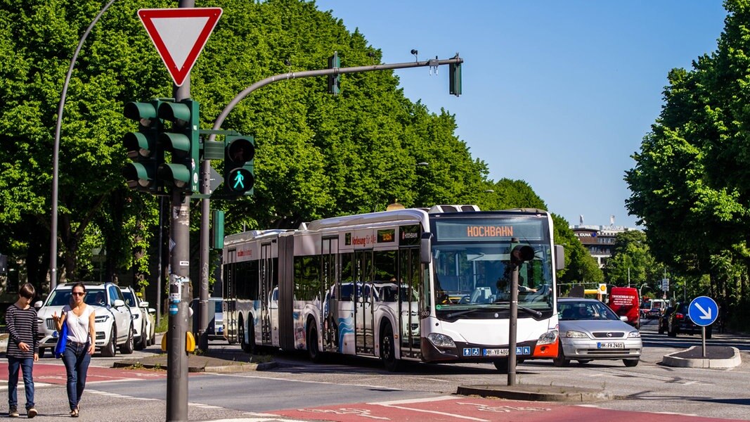 Ein Bus fährt in Hamburg über eine Kreuzung. Im Vordergrund gehen zwei Menschen über eine Fußgängerampel.