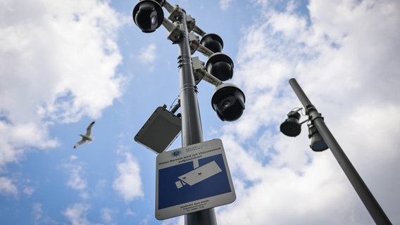 Ein Mast mit Überwachungskameras und einem Schild mit dem Text "Dieser Bereich wird mit Videotechnik aufgezeichnet" in Hamburg. © Christian Charisius/dpa 