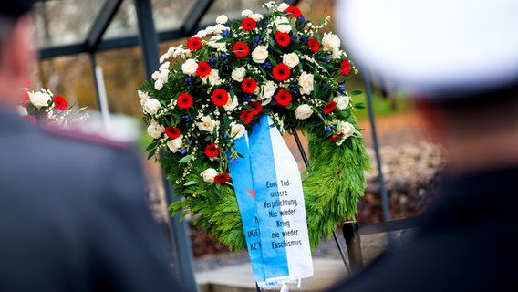 Ein Kranz mit der Aufschrift "Euer Tod - unsere Verpflichtung. Nie wieder Krieg. Nie wieder Faschismus." steht anlässlich des Volkstrauertages auf dem Gelände der KZ-Gedenkstätte Neuengamme. © dpa Foto: Daniel Bockwoldt