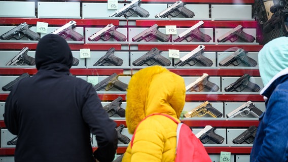 İnsanlar, alarm ve sinyal silahları satan bir silah dükkanının vitrininin önünde duruyor.  © dpa 