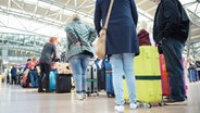 Reisende stehen im Terminal des Flughafen Hamburg mit ihren Rollkoffern in einer Warteschlange an einem Check in-Schalter. © picture alliance / dpa Foto: Gregor Fischer