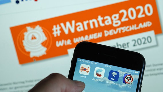 Verschiedene Warn-Apps, darunter die Notfall-Informations- und Nachrichten-App "Nina" des Bundesamts für Bevölkerungsschutz und Katastrophenhilfe, sind auf auf einem Smartphone vor einem Hinweis auf den "Warntag 2020" am 10. September zu sehen. © picture alliance/dpa/ZB Foto: Jens Kalaene