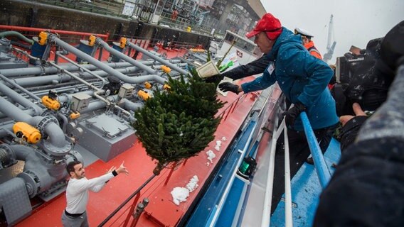 Michael Vosgerau wirft einen Tannenbaum vom Deck eines Ausflugsschiffes während der Aktion "Weihnachtsbäume für die Schiffe im Hamburger Hafen" in die Hände eines Seemann auf einem Tankschiff im Hamburger Hafen. © picture alliance / dpa Foto: Gregor Fischer