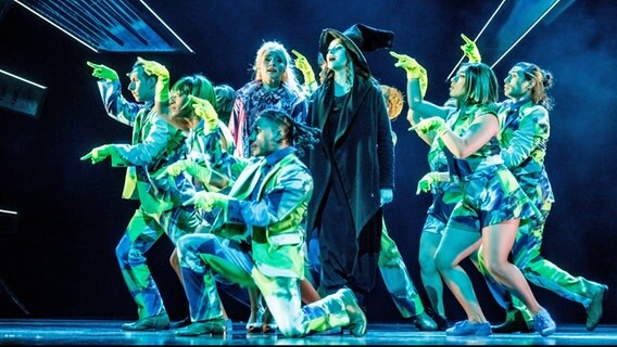 Die Sängerinnen Vajen van den Bosch (M, l.) als Elphaba und Jeannine Michele Wacker als Glinda singen und tanzen mit Ensemblemitgliedern bei einer Fotoprobe zu "Wicked" auf der Bühne des Hamburger Stage Theater Neue Flora. © picture alliance/dpa Foto: Markus Scholz