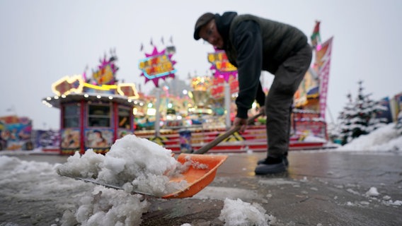 Ein Schausteller schiebt vor seinem Fahrgeschäft auf dem Hamburger Dom den Schnee beiseite. © picture alliance/dpa | Marcus Brandt Foto: Marcus Brandt