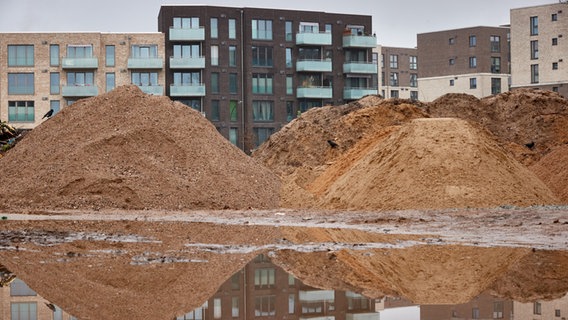 Blick auf Neubauten, die sich in einer Pfütze auf einer Baustelle in Hamburg spiegeln. © dpa Foto: Georg Wendt