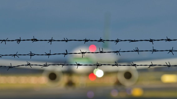 Auf einem Flughafen steht ein Flugzeug hinter Stacheldraht. © IMAGO Foto: Daniel Kubirski