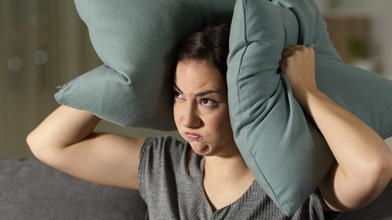 Eine Frau drückt sich gestresst zwei Kissen auf die Ohren. © Colourbox Foto: #81285