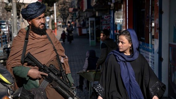 Ein Taliban-Kämpfer steht Wache, während eine Frau vorbeiläuft. © Ebrahim Noroozi/AP/dpa 