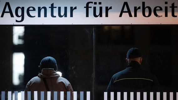 Zwei Menschen stehen im Dunklen vor einem Schild, auf dem "Agentur für Arbeit" steht. © dpa Foto: Marijan Murat