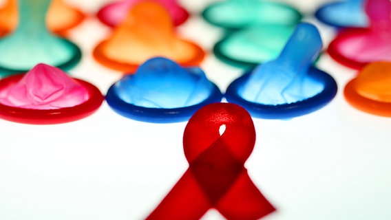 Eine Aidsschleife und Kondome liegen auf einem Leuchttisch. © dpa Foto: Oliver Berg
