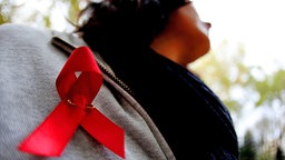 Eine Aids-Schleife hat sich eine Frau an die Brust geheftet. © dpa Foto: Oliver Berg