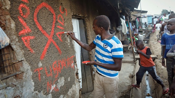 Ein junger Mann malt eine rote Aids-Schleife auf eine Wand im Kibera-Slum und schreibt in roten Buchstaben den Slogan "Avoid AIDS". © dpa picture alliance Foto: Dai Kurokawa
