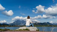 Eine Frau sitzt an einem See auf einem Stein © picture alliance / Westend61 Foto: Daniel Ingold
