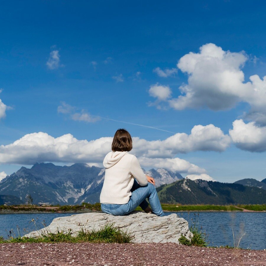 Eine Frau sitzt an einem See auf einem Stein © picture alliance / Westend61 Foto: Daniel Ingold