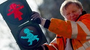 Ein Techniker hält eine Ampel, auf der zwei Ampelfrauen in den Farben Rot und Grün zu sehen sind. © dpa picture alliance Foto: Patrick Pleul