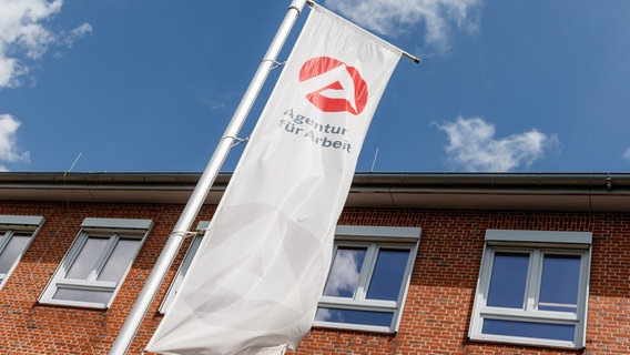 Vor der Agentur für Arbeit in Lüneburg weht eine Fahne mit dem Logo der Arbeitsagentur. © picture alliance / dpa Themendienst Foto: Markus Scholz