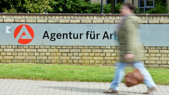 Eine Frau läuft an einem Schild mit der Aufschrift "Agentur für Arbeit" vorbei. © dpa picture alliance Foto: Carsten Rehder