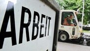 Ein Mann reinigt neben einem Schriftzug der Bundesagentur für Arbeit in Hannover eine Straße mit einer Kehrmaschine. © dpa Foto: Julian Stratenschulte