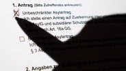 Der Schatten eines Kugelschreibers zeichnet sich auf einem schriftlichen Asylerstantrag des Bundesamt für Migration und Flüchtlinge (BAMF) ab. © dpa Foto: Julian Stratenschulte