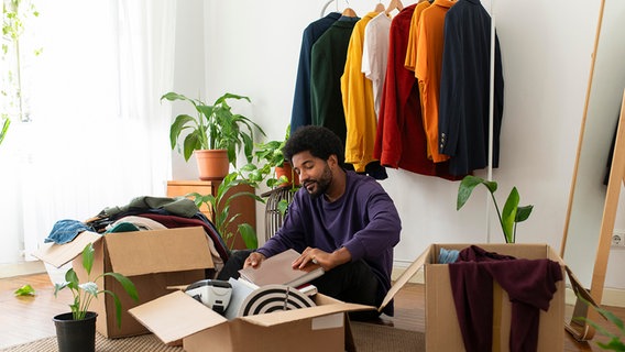 Ein Mann sortiert Kleidung und Gegenstände in einem Wohnraum aus. © picture alliance Foto: Victoria Rayu