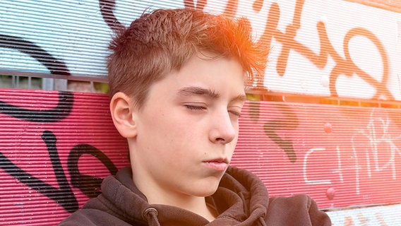 Ein Jugendlicher mit geschlossenen Augen lehnt an einer mit Graffiti besprühten Wand © photocase.de Foto: Armin Staudt-Berlin