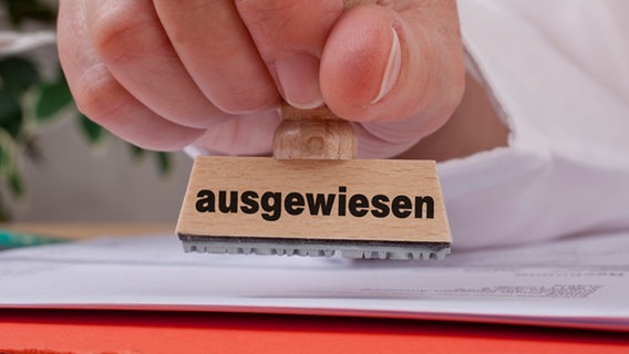 Eine Hand hält einen Stempel mit der Aufschrift "ausgewiesen". © picturedesk.com Foto: Christian Ammering