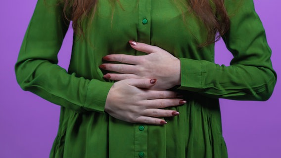 Eine Frau in Bluse hält sich mit beiden Händen den Bauch © Colourbox Foto: Stock Holm