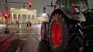 Ein Traktor steht im Dunklen in Berlin in der Nähe des erleuchteten Brandenburger Tors auf einer Straße. © dpa bildfunk Foto: Jörg Carstensen