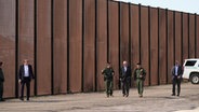 Joe Biden (M), Präsident der USA, besucht die Grenze zwischen den USA und Mexiko und geht mit US-Grenzschutzbeamten entlang eines Abschnitts am Grenzzaun in El Paso, Texas. © Andrew Harnik/AP/dpa 