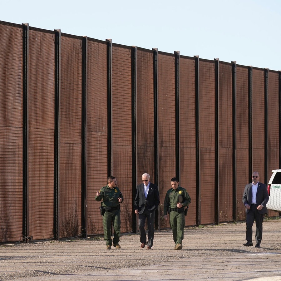 Joe Biden (M), Präsident der USA, besucht die Grenze zwischen den USA und Mexiko und geht mit US-Grenzschutzbeamten entlang eines Abschnitts am Grenzzaun in El Paso, Texas. © Andrew Harnik/AP/dpa 
