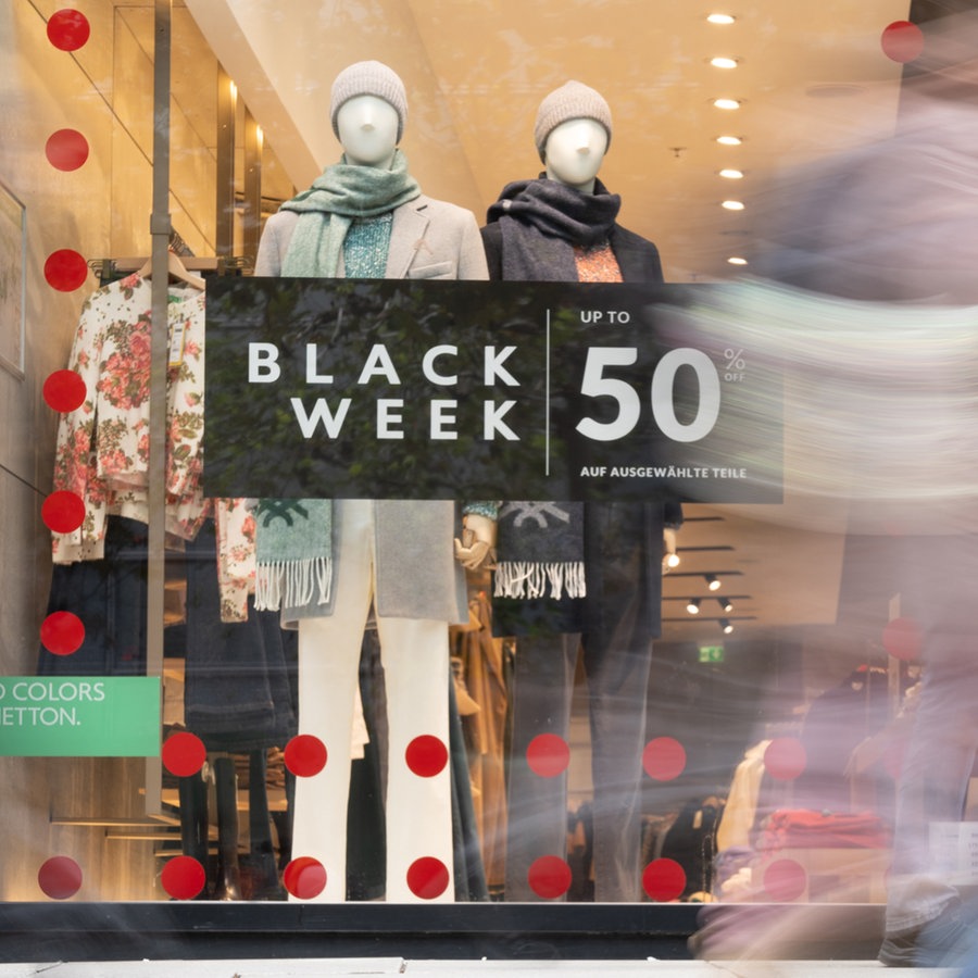 Werbung für den "Black Week Sale" hängt in einem Schaufenster, an dem Passanten vorbeigehen © picture alliance/dpa Foto: Etienne Dötsch