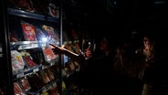 Menschen in Spanien kaufen während eines massiven Stromausfalls in einer Kühltheke im Supermarkt ein, beleuchtet durch ihre Smartphone-Kameras. © picture alliance/dpa/AP Foto: Miguel Oses