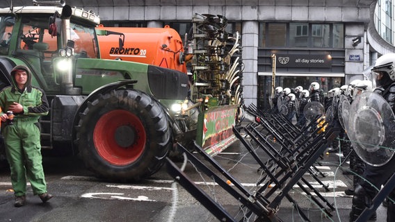Polizisten stehen im Brüsseler Europaviertel hinter einer Barrikade, auf der anderen Seite stehen zwei Traktoren von Landwirten. © dpa-Bildfunk/AP Foto: Harry Nakos