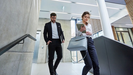 A man and a woman are hurrying down the stairwell of an office building.  © dpa picture alliance / Zoonar Photo: Robert Kneschke