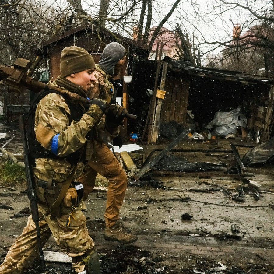Ukrainische Soldaten inspizieren die Trümmer einer zerstörten russischen Panzerkolonne auf einer Straße in Butscha, einem Vorort nördlich der Hauptstadt. © picture alliance/dpa/SOPA Images via ZUMA Press Wire | Matthew Hatcher 