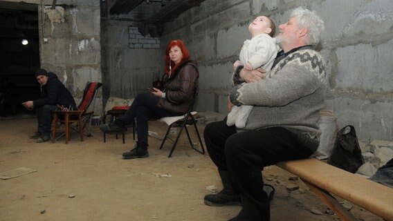 Ein Mann mit einem Baby sitzt mit anderen Ukrainern in Charkiw im Keller eines Wohnhauses. © dpa-Bildfunk 